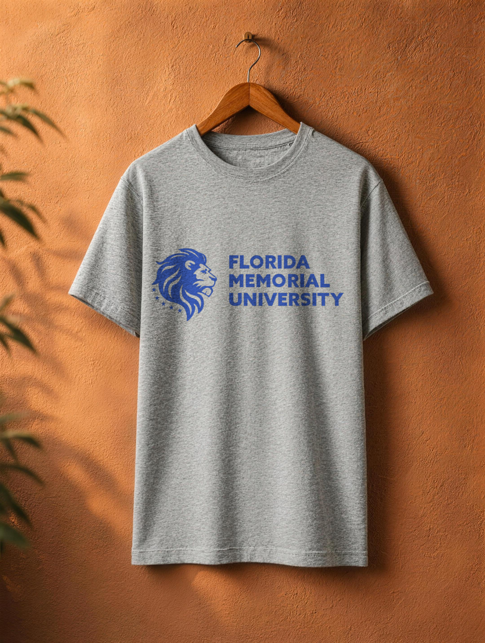 Florida Memorial University Stacked Wordmark tee in athletic heather on a wooden hanger against a textured terracotta wall